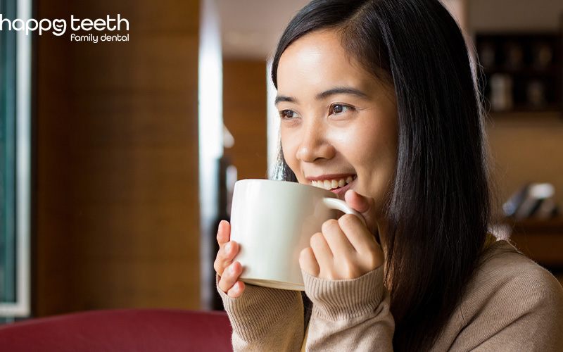 Smiling woman holding a white mug about to drink a hot beverage indoors Smiling woman holding a white mug about to drink a hot beverage indoors