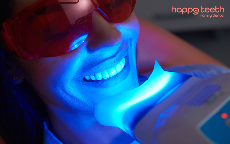 Woman receiving professional teeth whitening treatment using a blue LED light Woman receiving professional teeth whitening treatment using a blue LED light